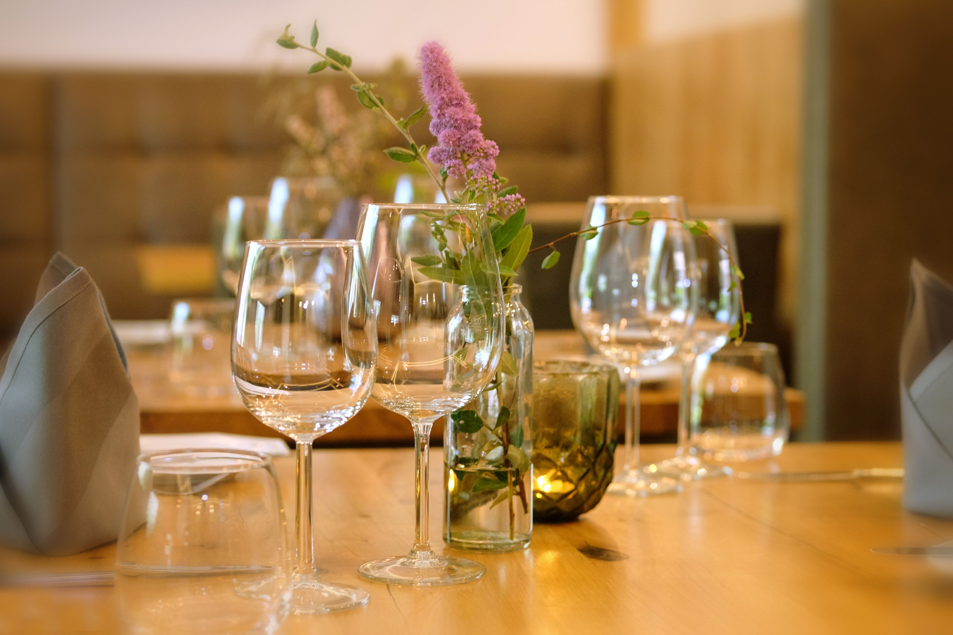 A dining table with several wine glasses and a vase with a purple flower.