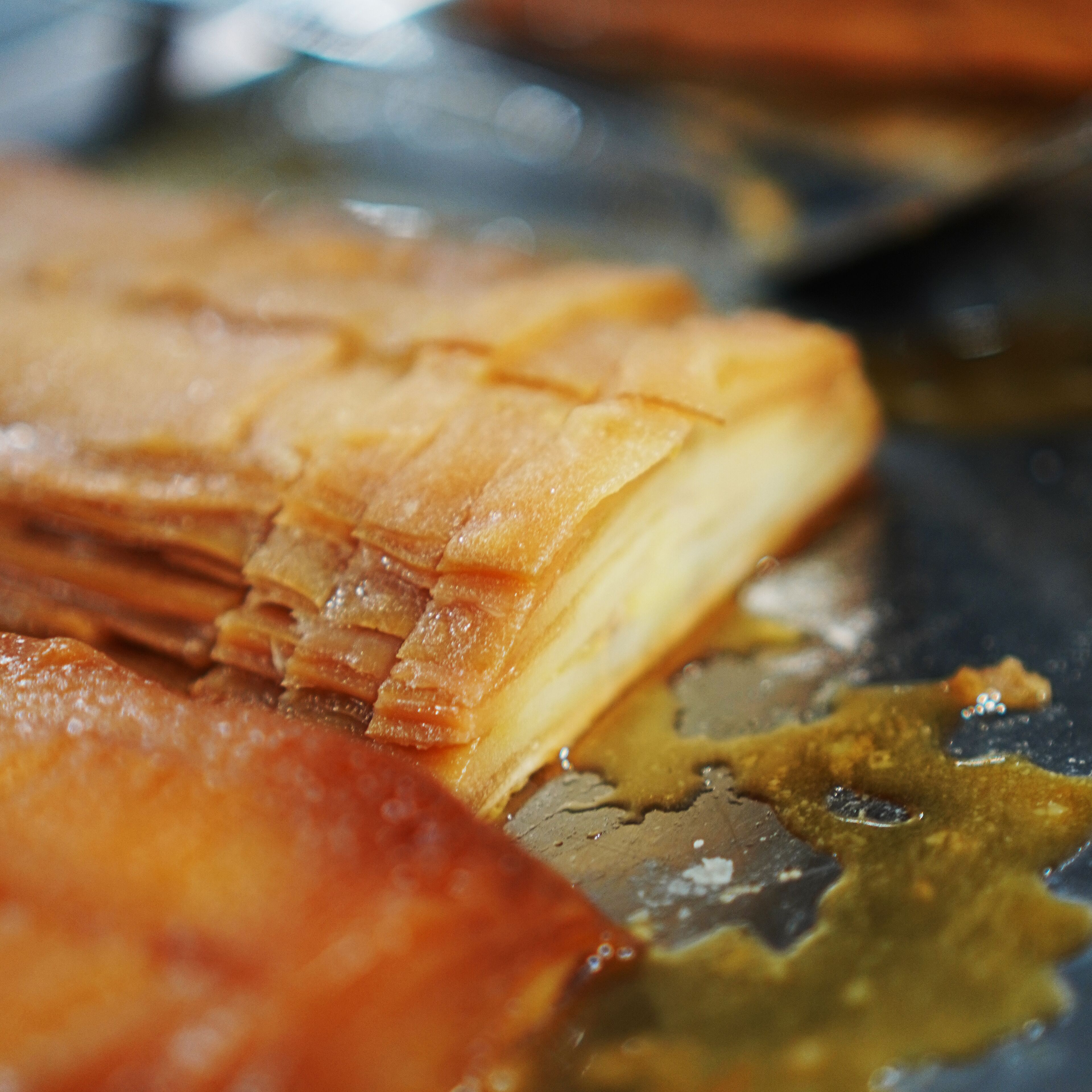 Primer plano de un alimento con corteza dorado-marrón, posiblemente un pastel o producto horneado, con capas visibles y superficie brillante.