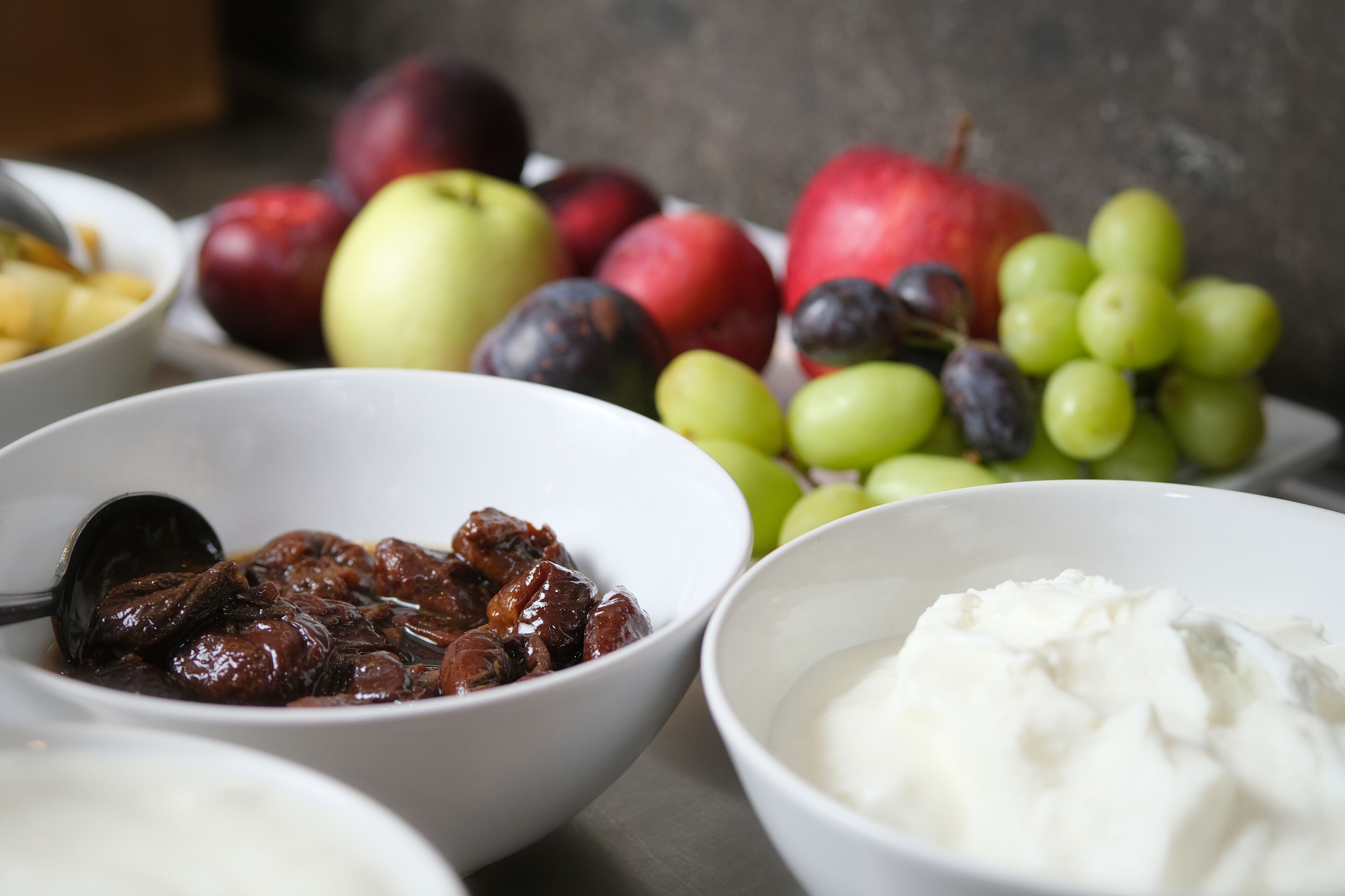 Una mesa con recipientes de comida que incluyen dátiles, uvas, manzanas y yogur.