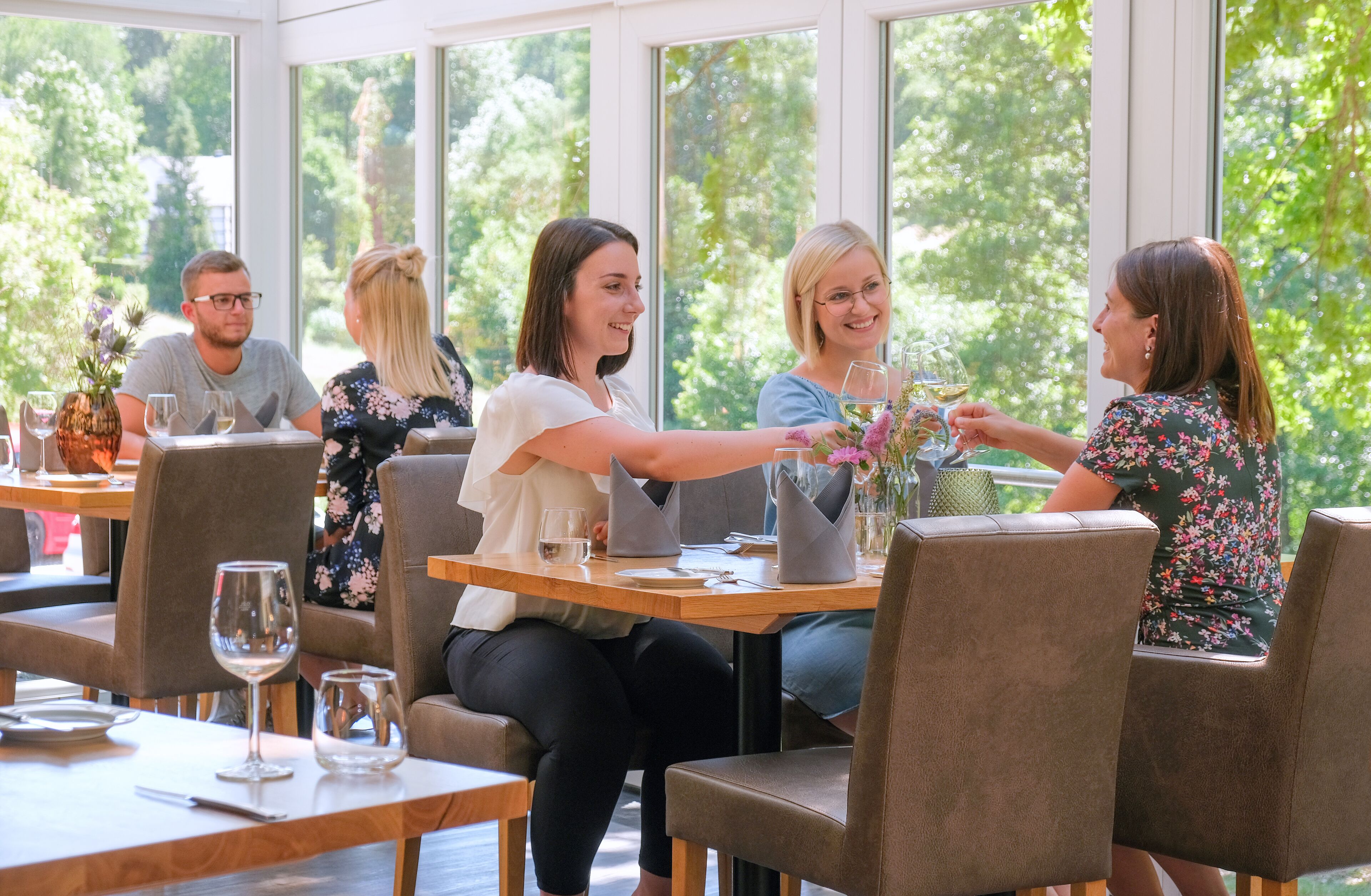 Un grupo de personas sentadas en una mesa en un restaurante con ventanas amplias y vistas a zonas verdes.