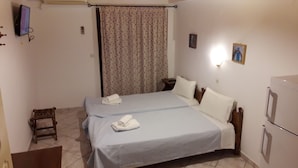 A bedroom with two beds, a television, a small table, and a refrigerator. - Myrtoo (Monemvasia)