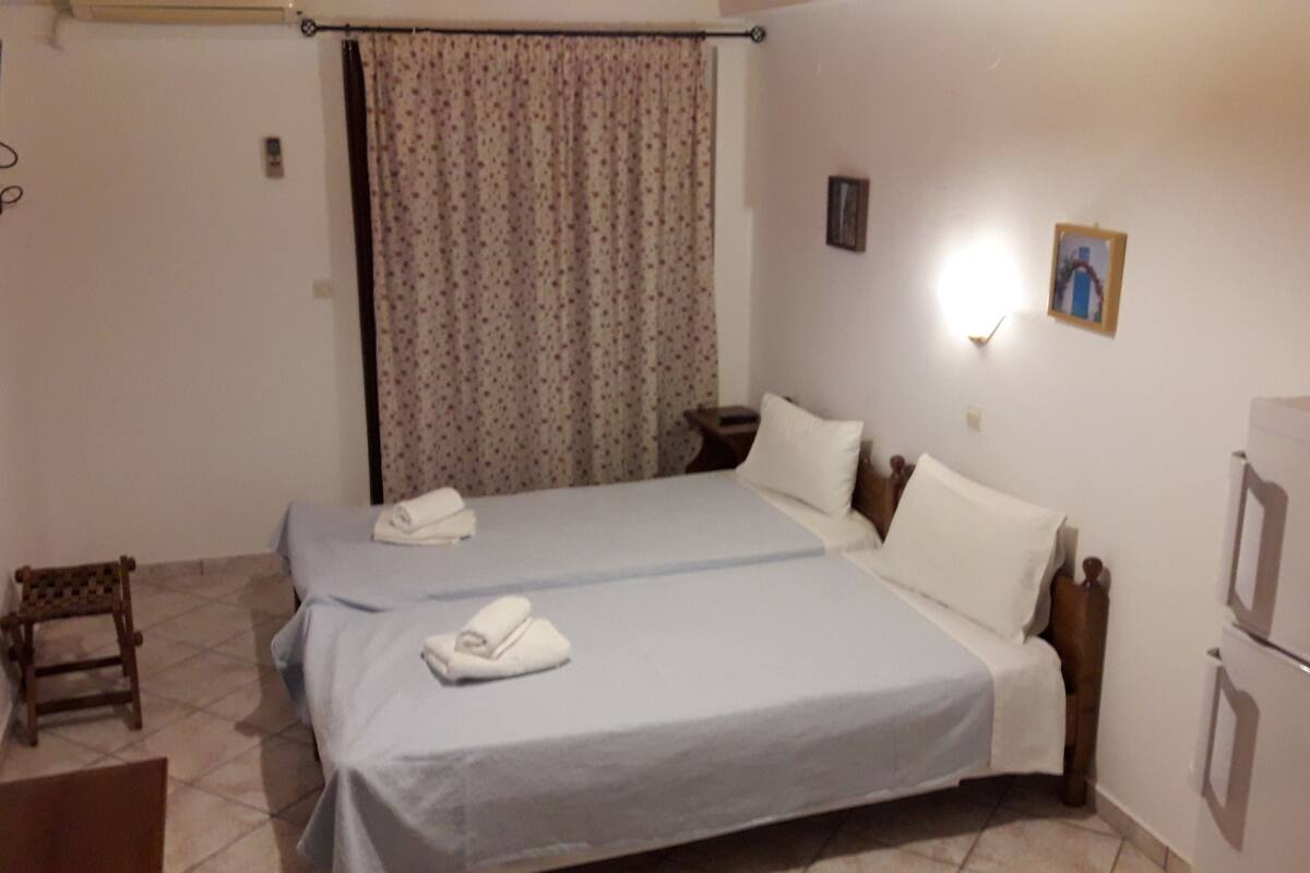 A bedroom with two beds, a television, a small table, and a refrigerator.