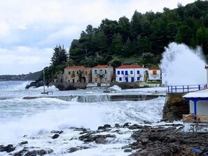 Escena costera con costa rocosa, una serie de edificios de arquitectura tradicional y un mar agitado.