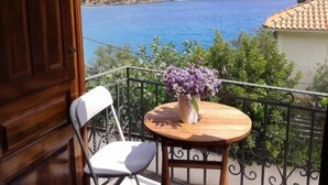 A balcony with a view of a lake, a chair, and a table with a vase of flowers. - Myrtoo (Monemvasia)