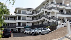 A multi-story hotel with balconies, a covered entrance, and a parking area with several cars. - Setra Priangan Guesthouse (Bandung)