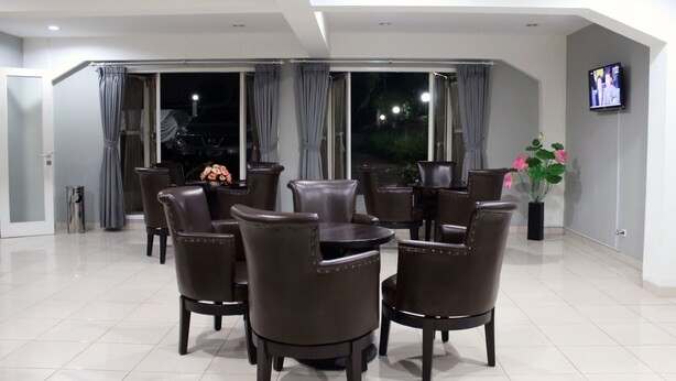 A modern dining area with brown leather chairs and tables, large windows with curtains, and a flat-screen TV on the wall. - Setra Priangan Guesthouse (Bandung)