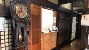 A traditional wooden reception desk with a clock, a wooden door, and a calendar on the wall. - Sosuke (Takayama)