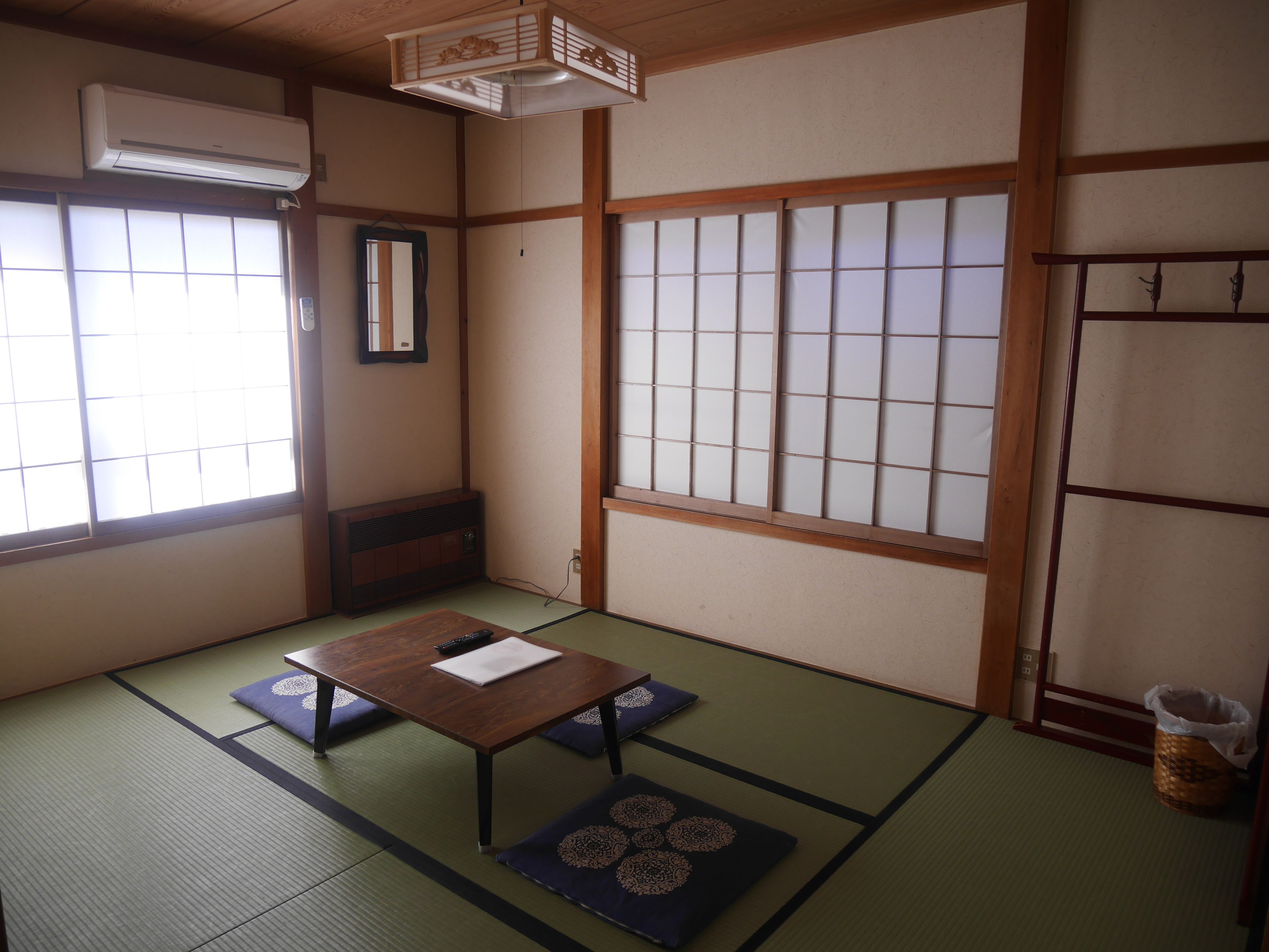 A traditional Japanese room with tatami flooring, shoji screens, a wooden table with cushions, and a hanging lantern.