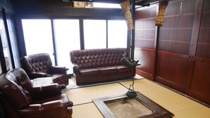 A traditional tatami mat room with a brown leather sofa, a small tatami mat table, and a decorative fish on a stand. - Sosuke (Takayama)