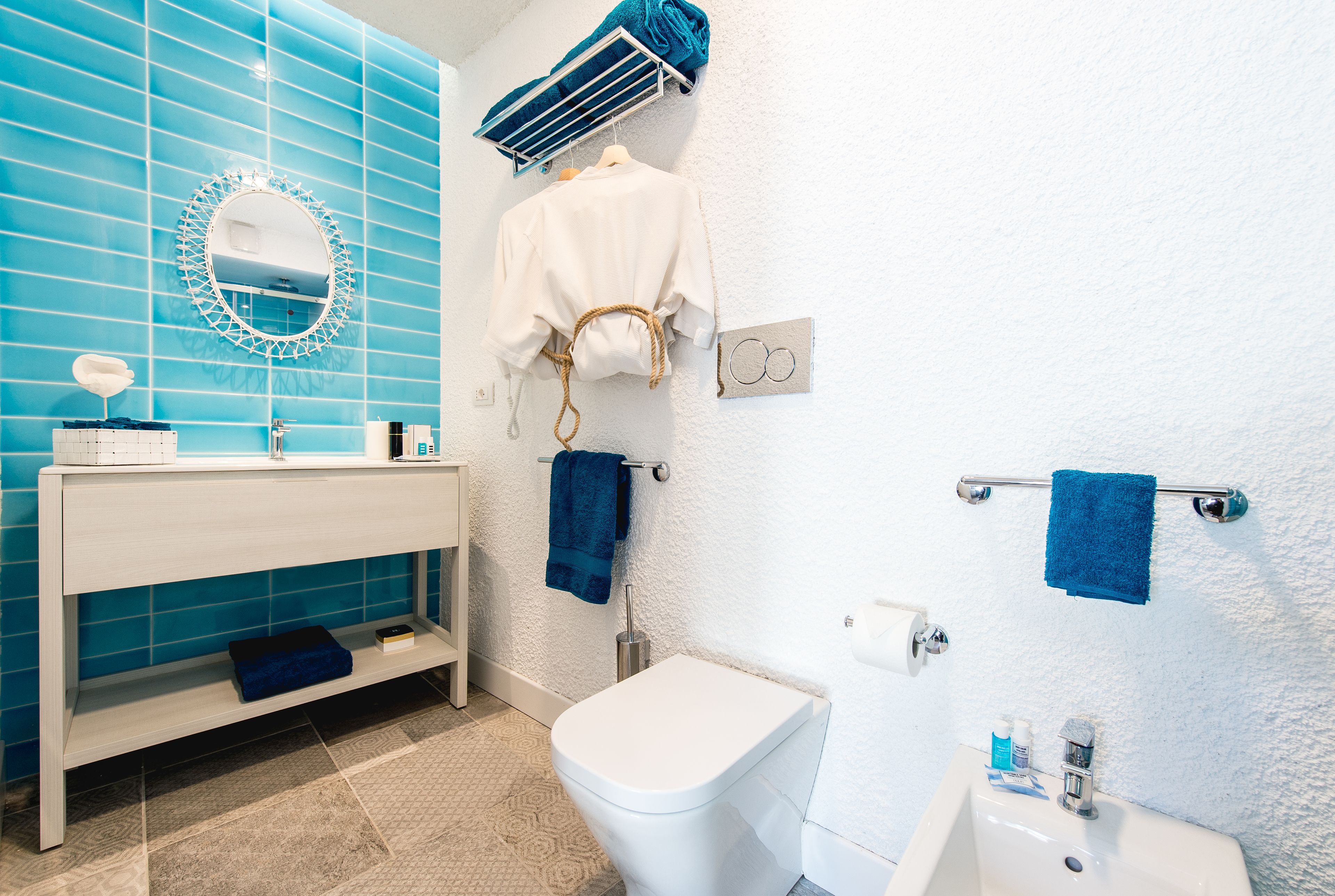 A bathroom with a white sink, blue-tiled walls, a white toilet, and a blue towel rack.