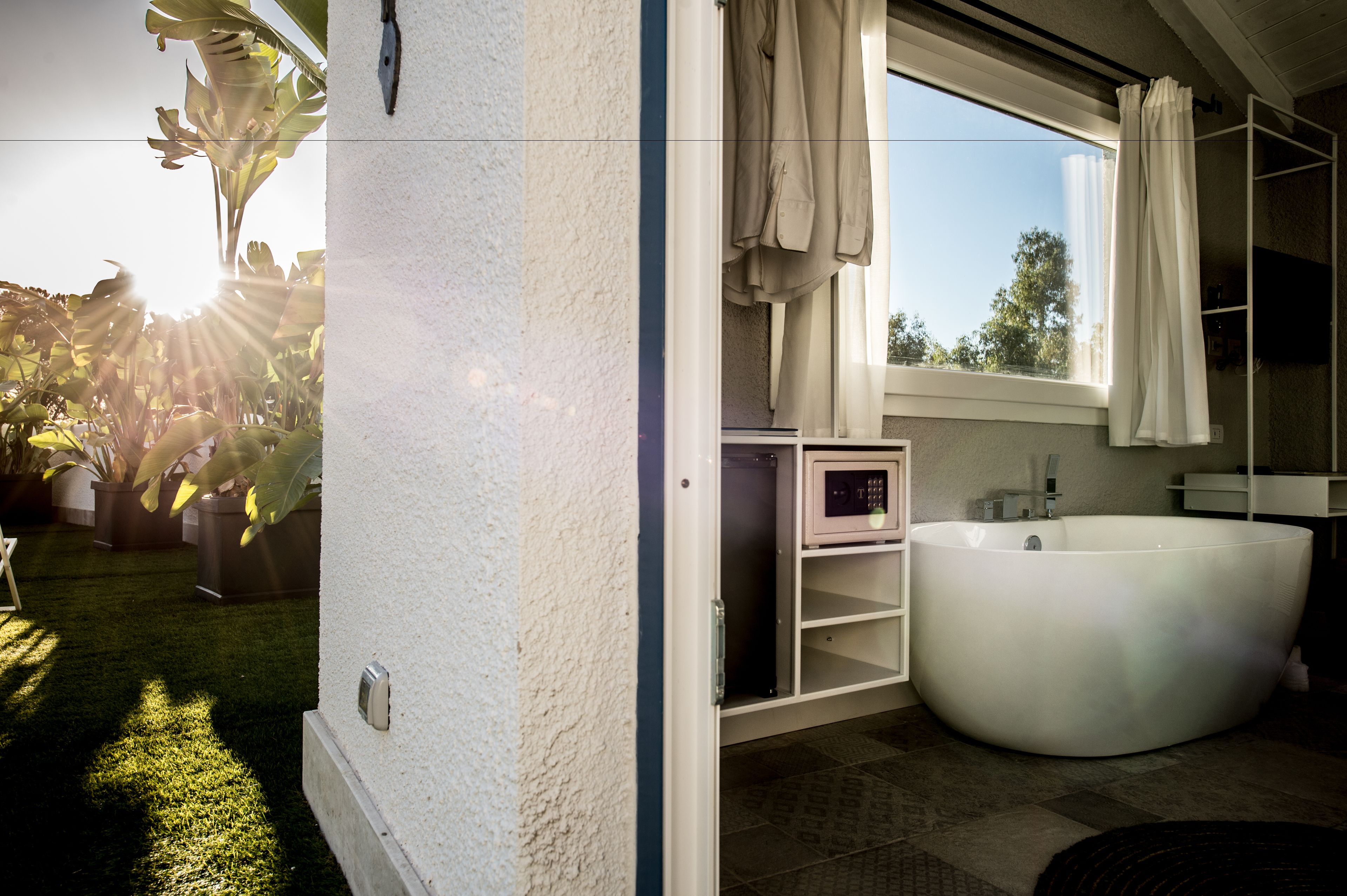 Un baño moderno con una bañera grande, ducha y retrete. Hay una ventana con cortinas y un estante pequeño con artículos de aseo.