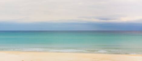 A beach with clear turquoise water, sandy shore, and large rocks.