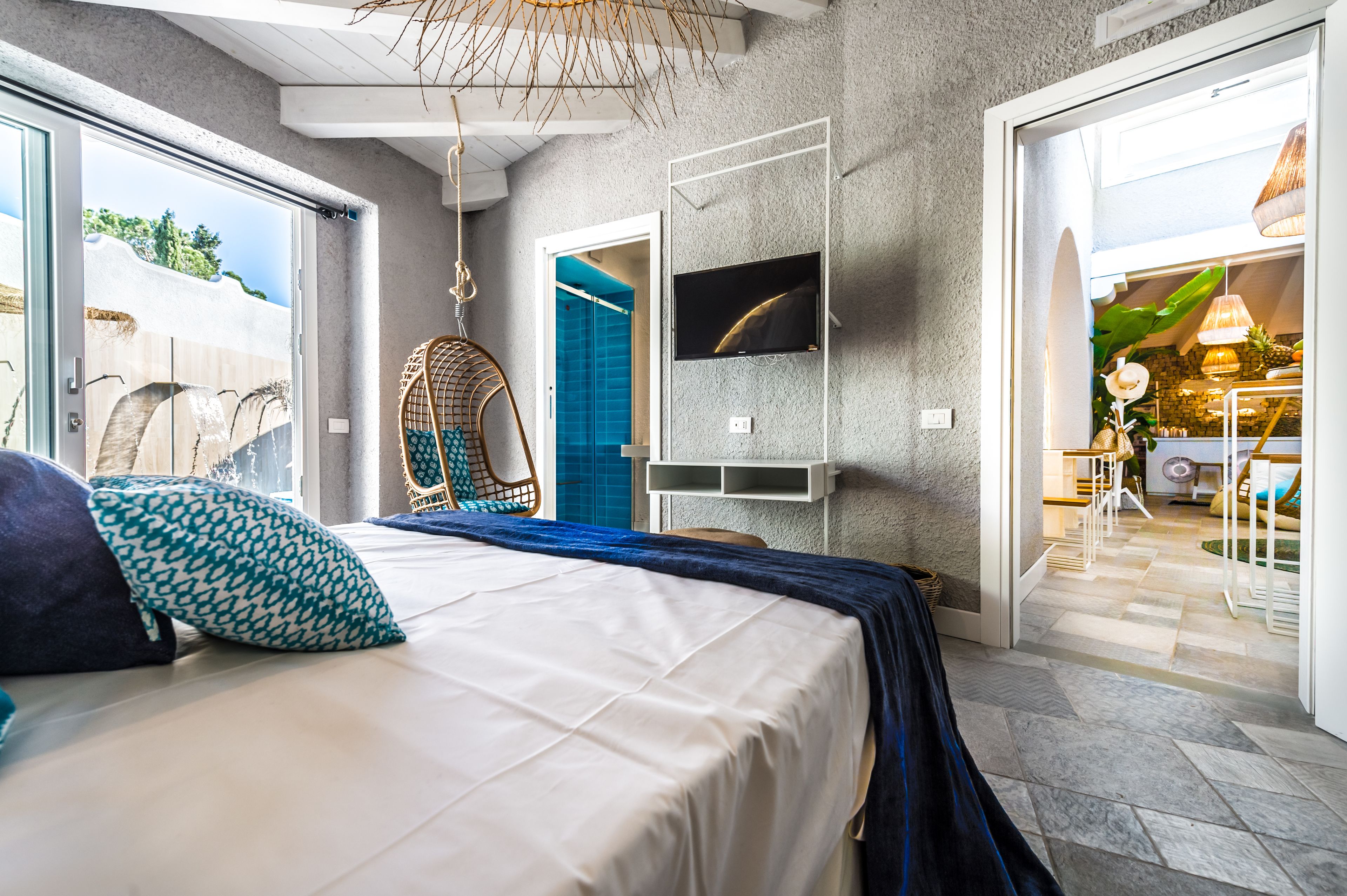 A bedroom with a bed, a hanging chair, a TV, and a view of the outside.