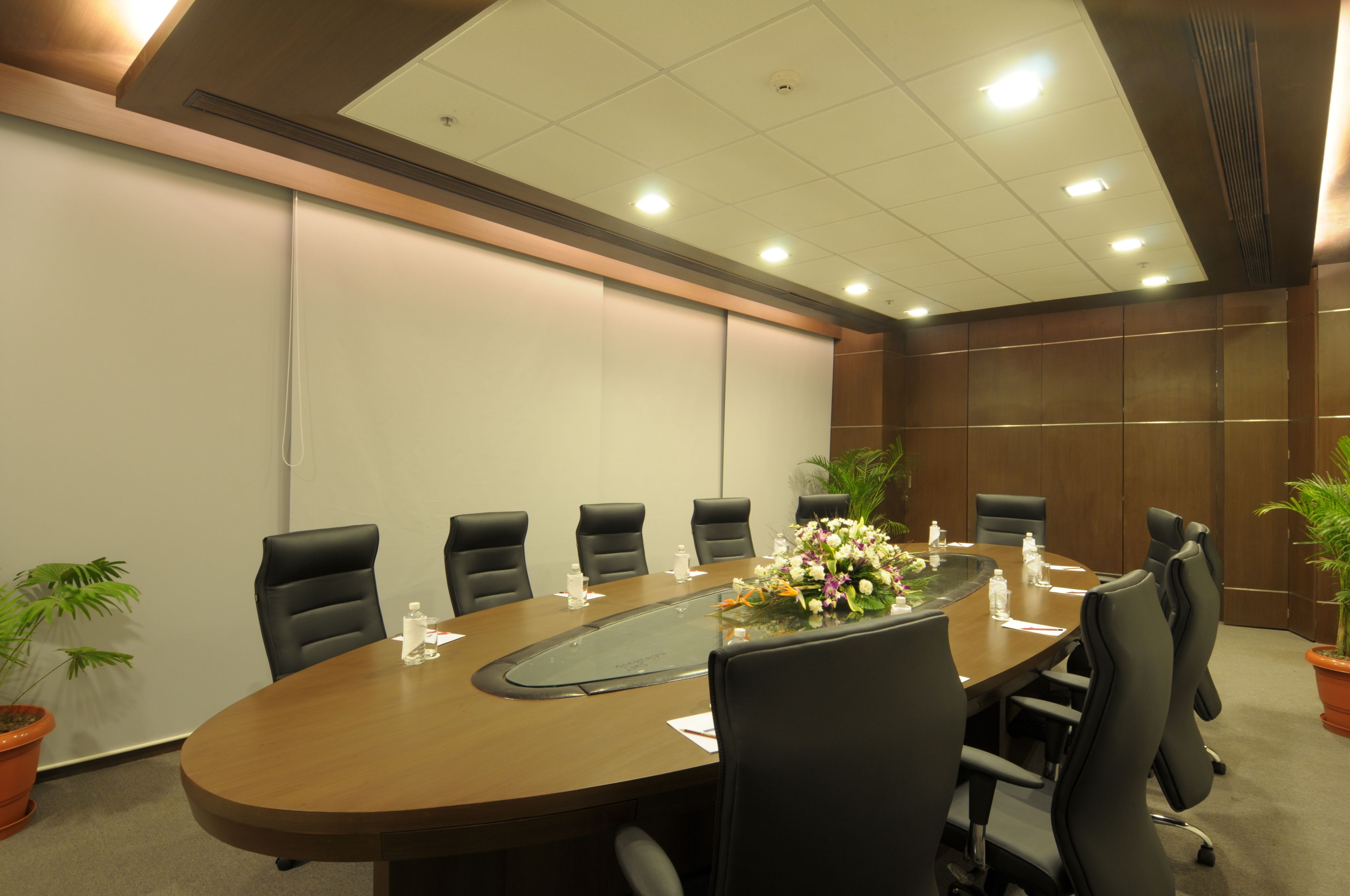 Una sala de conferències amb una taula llarga, cadires negres i plantes en testos.