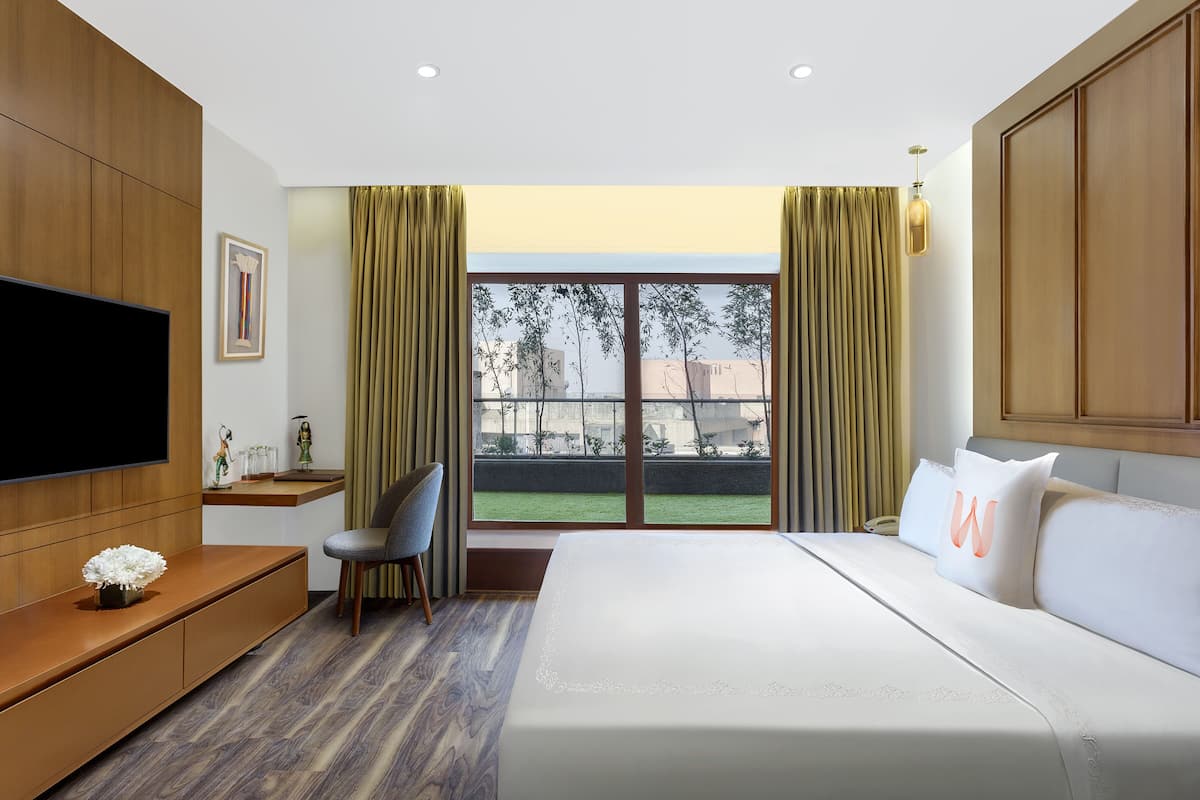 Habitación de hotel moderna con una cama grande, televisión, escritorio y vistas al exterior.