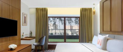 A modern hotel room with a large bed, a TV, a desk, and a view of the outdoors.