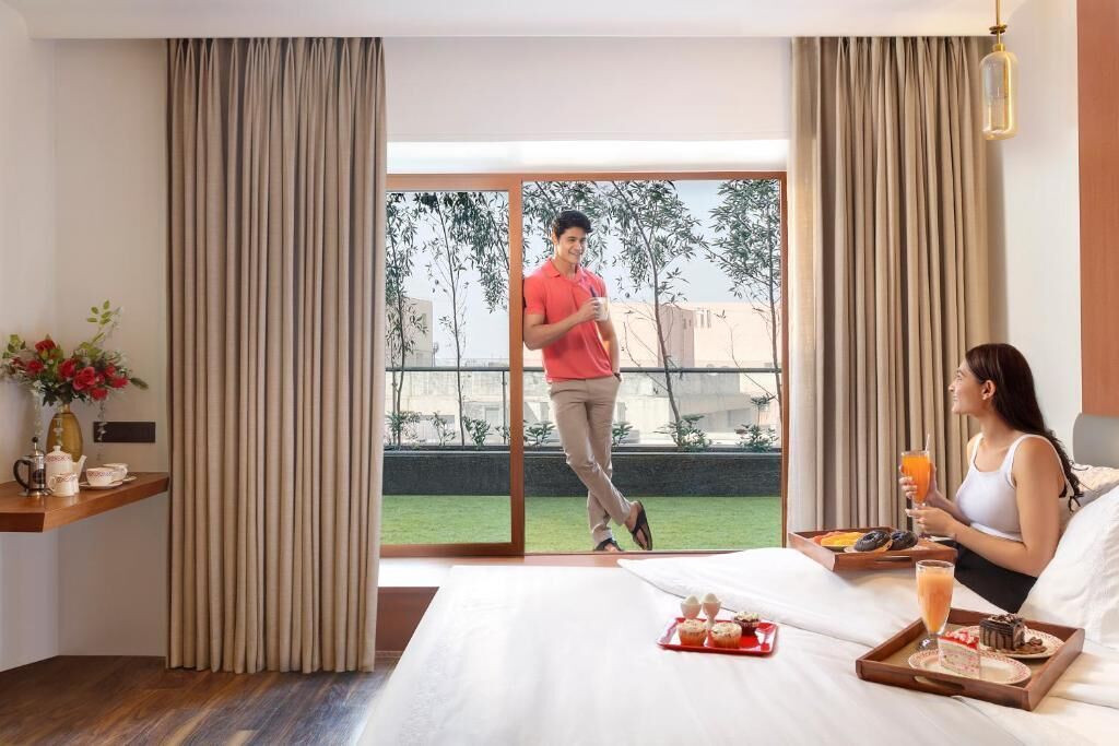 Habitación de hotel con cama, bandeja de desayuno y vistas a un balcón donde hay una persona.