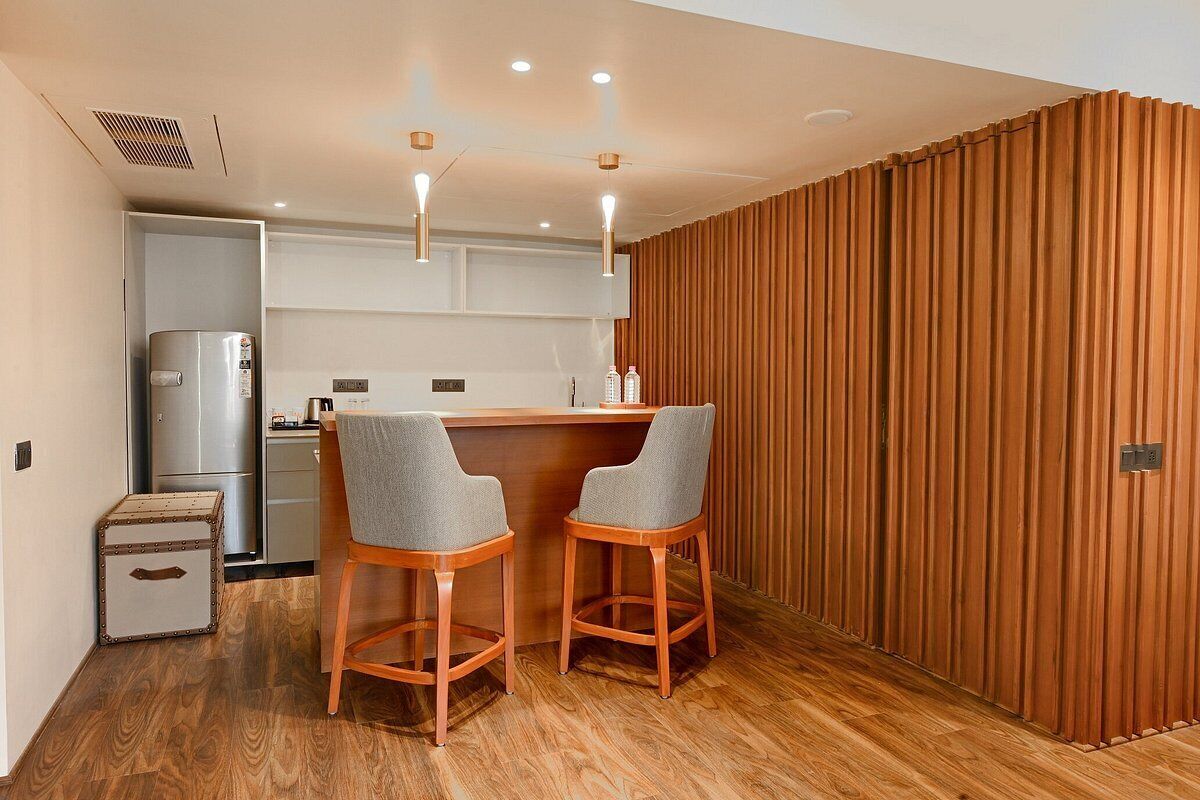 A compact kitchen with a wooden bar area, two bar stools, and a refrigerator.