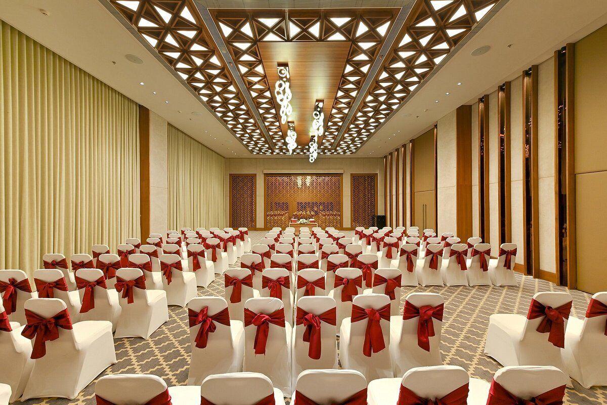 A conference room with rows of white chairs with red sashes, a patterned carpet, and a decorative ceiling.