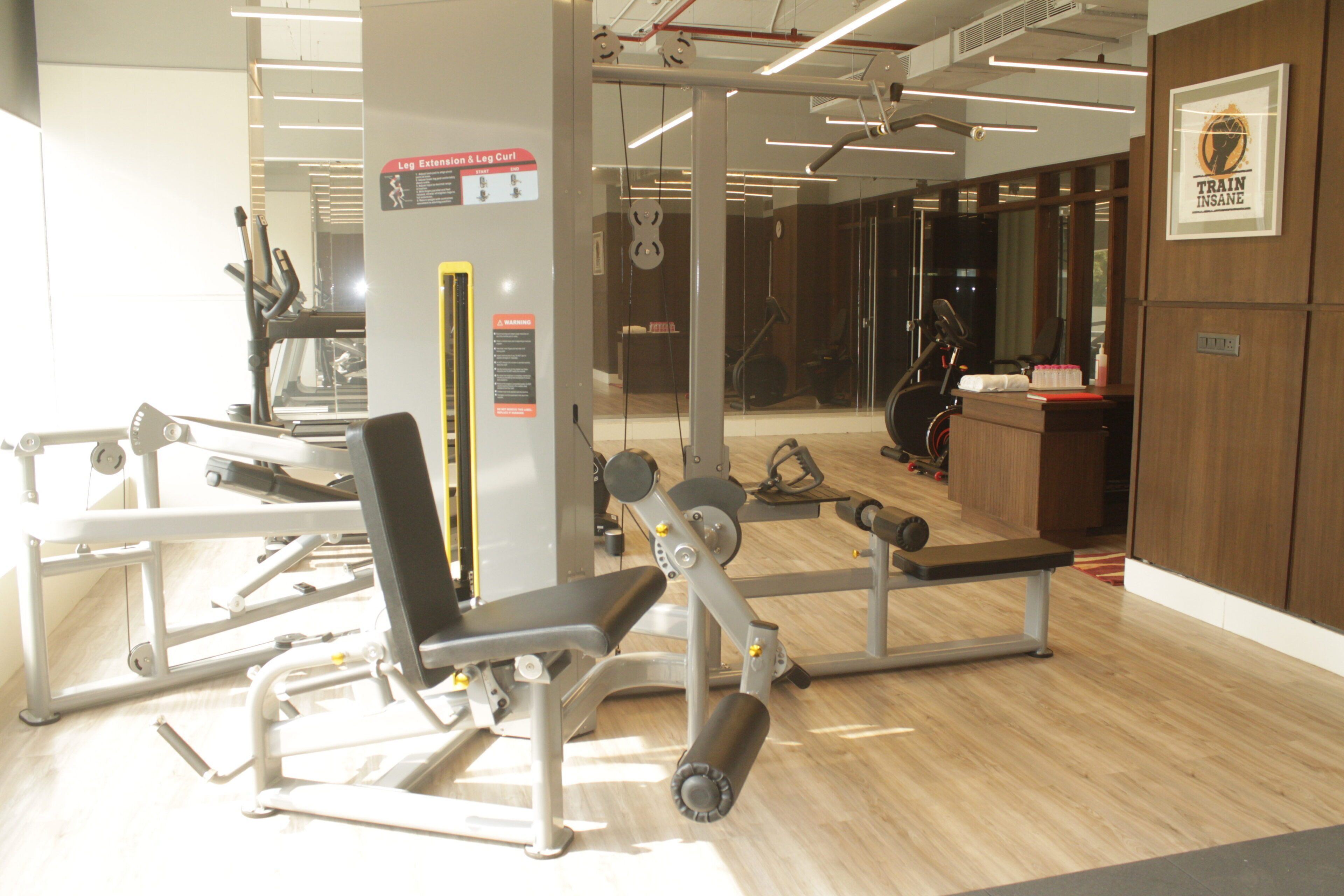 Une salle de sport équipée de divers appareils d’exercice, d’un miroir et d’un panneau indiquant l’emplacement des appareils d’extension et de flexion des jambes.