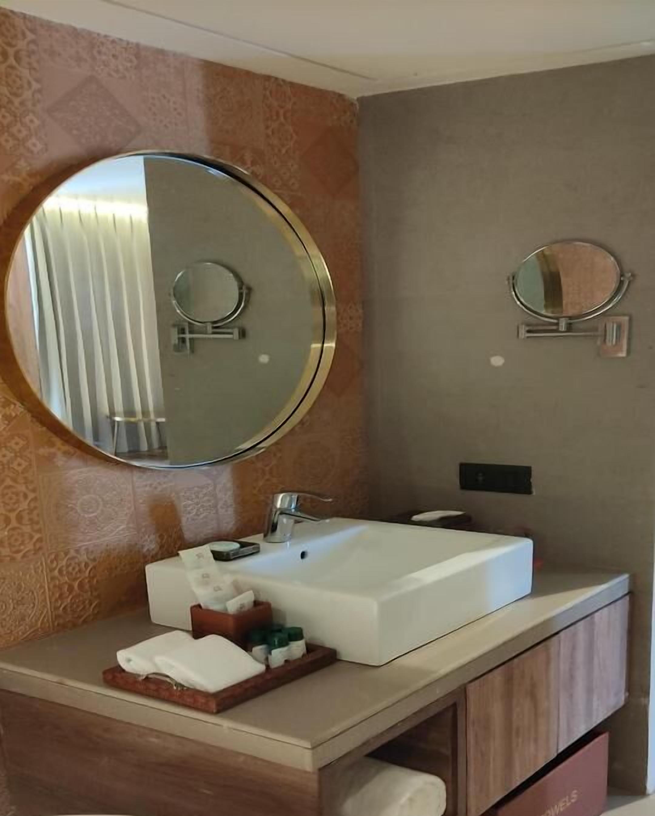 A bathroom with a large round mirror, a rectangular sink, and a vanity with a mirror.