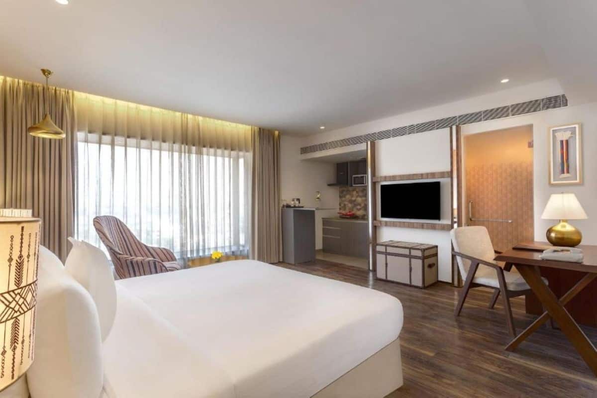 Habitación de hotel con una cama grande, un escritorio con lámpara, televisión y kitchenette.