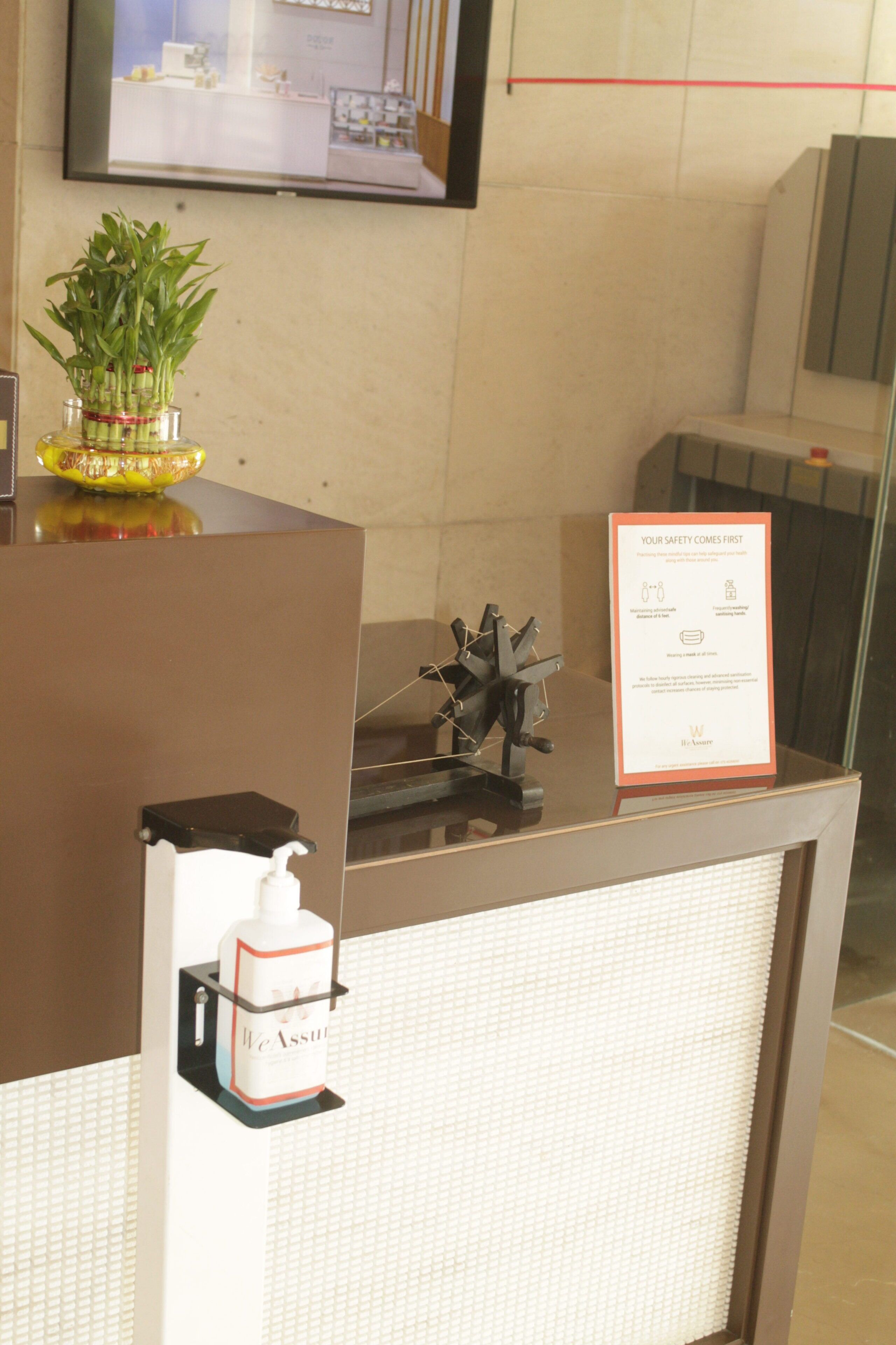 A reception desk with a framed safety notice, a small plant, and a hand sanitizer dispenser.