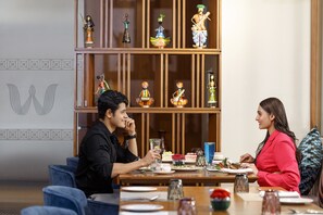 Un coin repas avec une table en bois dressée pour deux personnes, entourée d’objets décoratifs et agrémentée d’un mur à motifs.