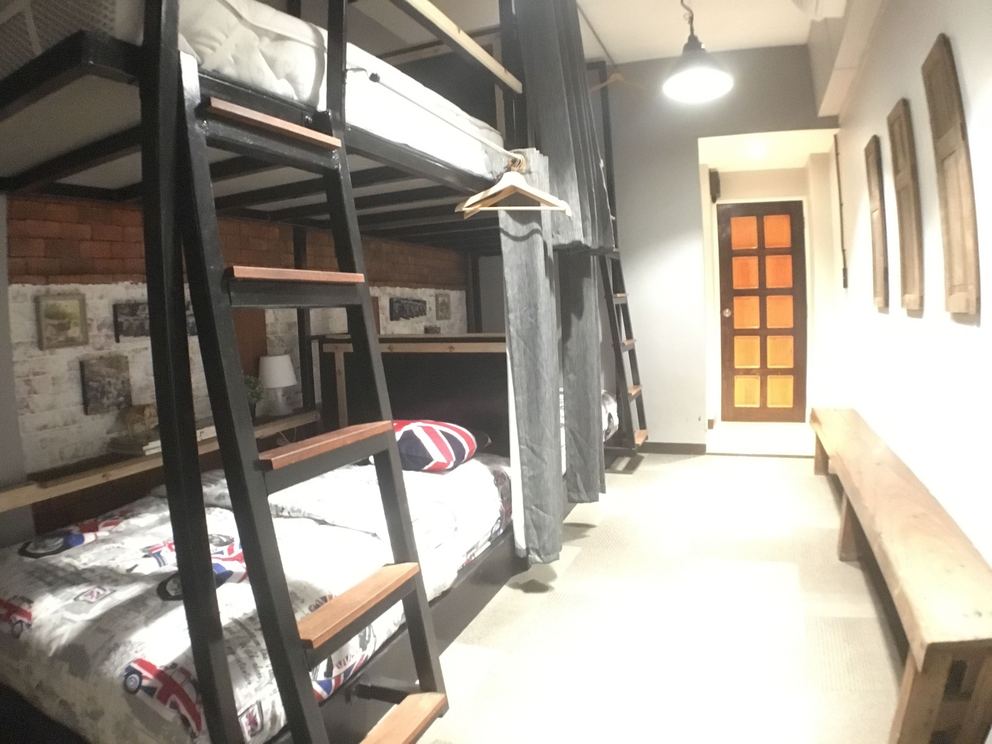 A dormitory room with bunk beds, a wooden bench, a door with glass panels, and a brick wall with pictures.