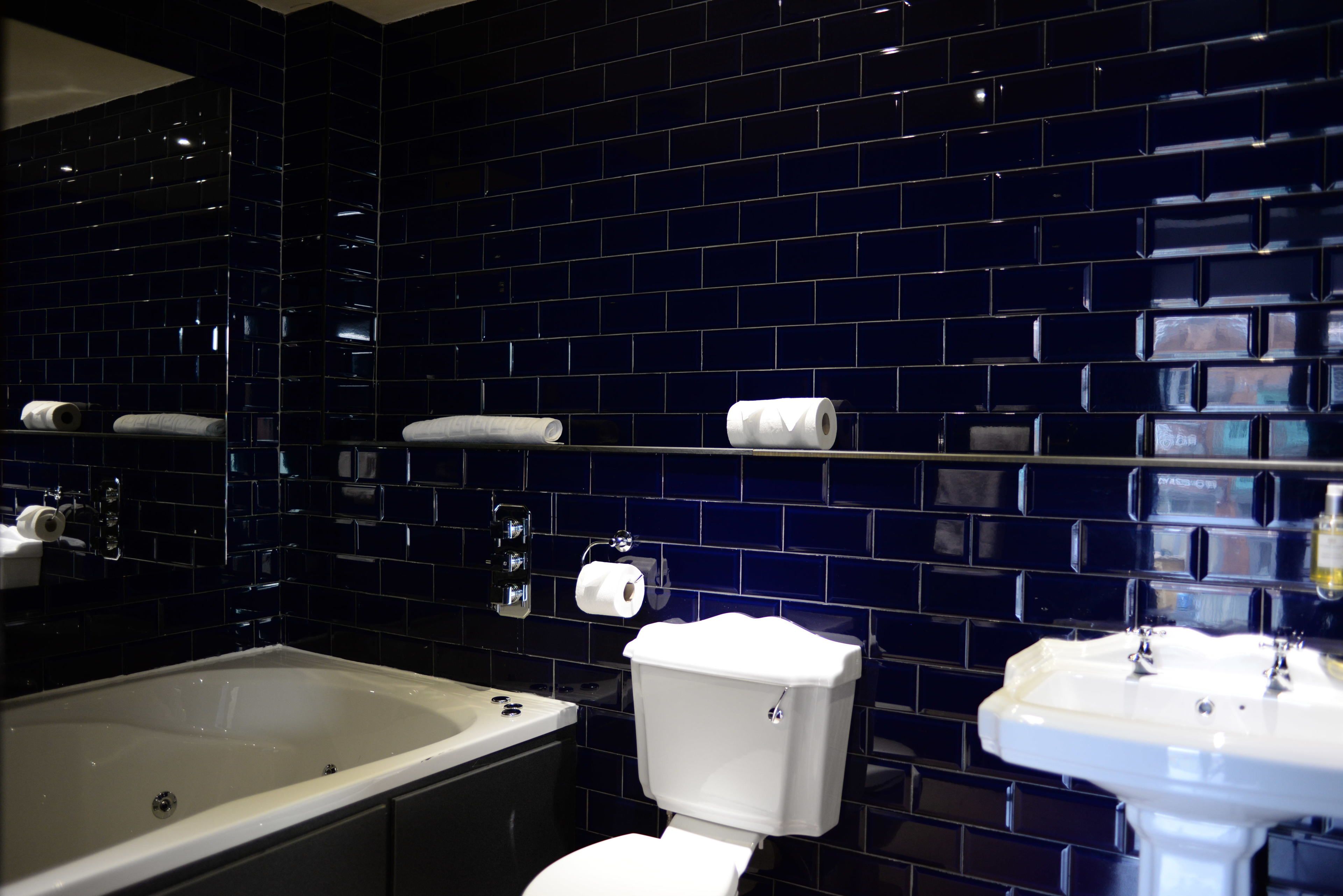 A bathroom with a bathtub, toilet, and sink, all with white fixtures against a dark blue tiled wall.