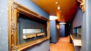 Un couloir avec un mur bleu, un grand miroir doré à motifs et un plancher en bois.