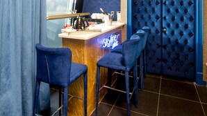 Un coin bar agrémenté d’une tête de lit bleue à motifs capitonnés, de tabourets de bar et d’un comptoir orné d ’une enseigne au néon.