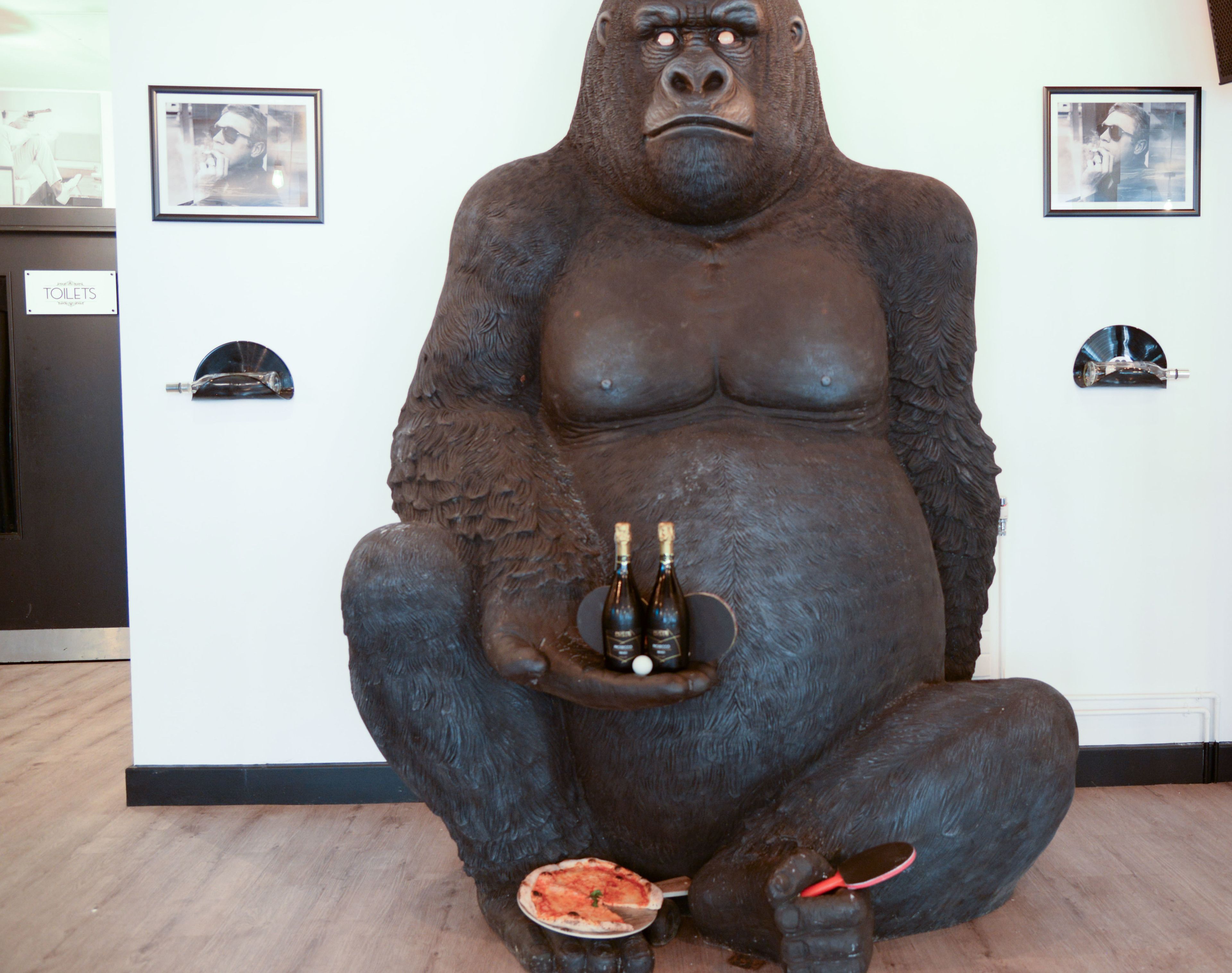 A large gorilla statue holding a bottle and a pizza slice.