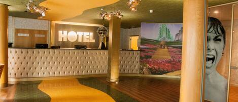 A hotel reception area with a 'HOTEL' sign, a reception desk, a large mural, and a unique floor design.