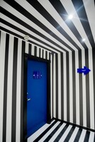 A hallway with black and white striped walls, a blue door with a number plate, and a directional sign.