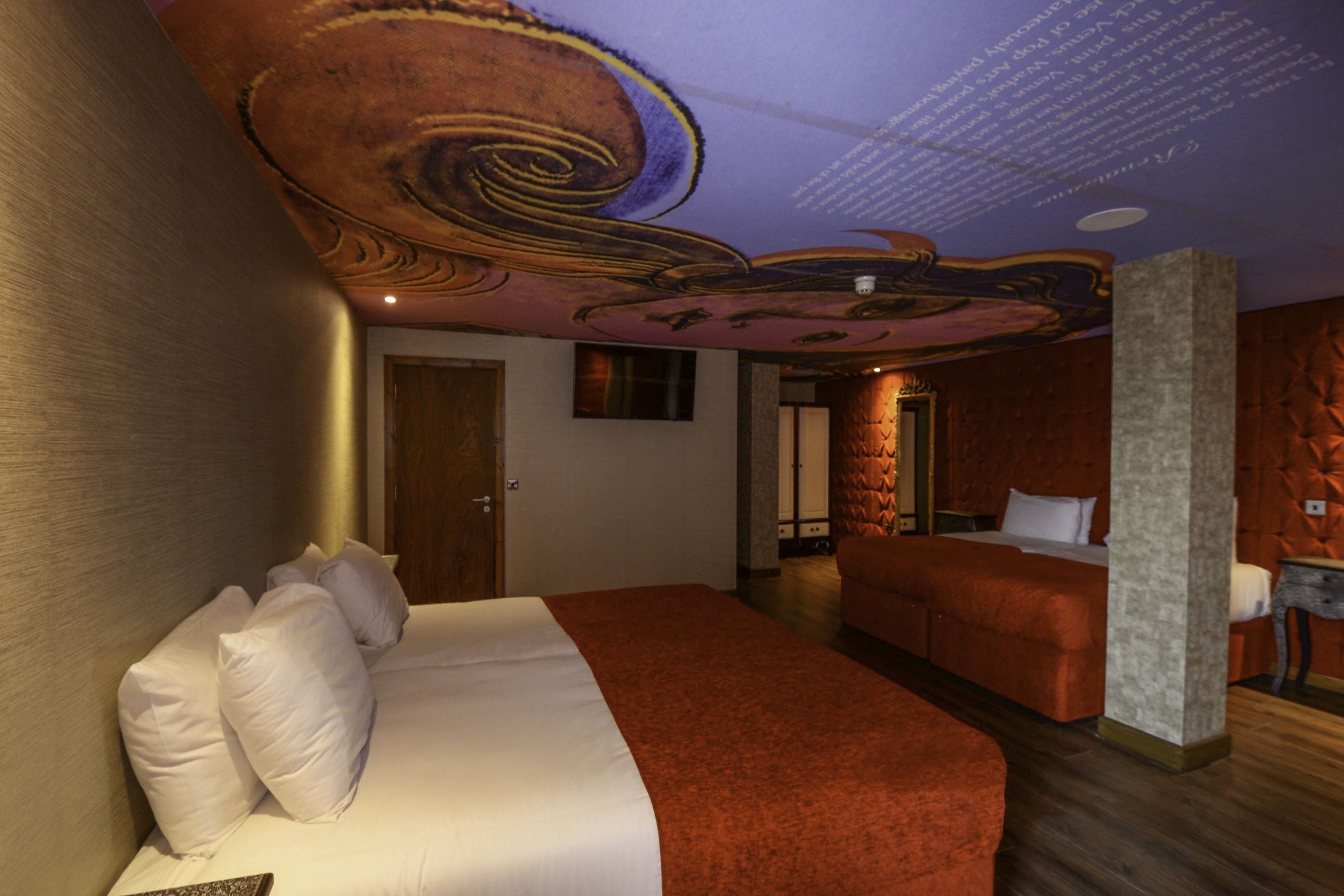 A hotel room with a large bed, a smaller bed, and a unique ceiling design.