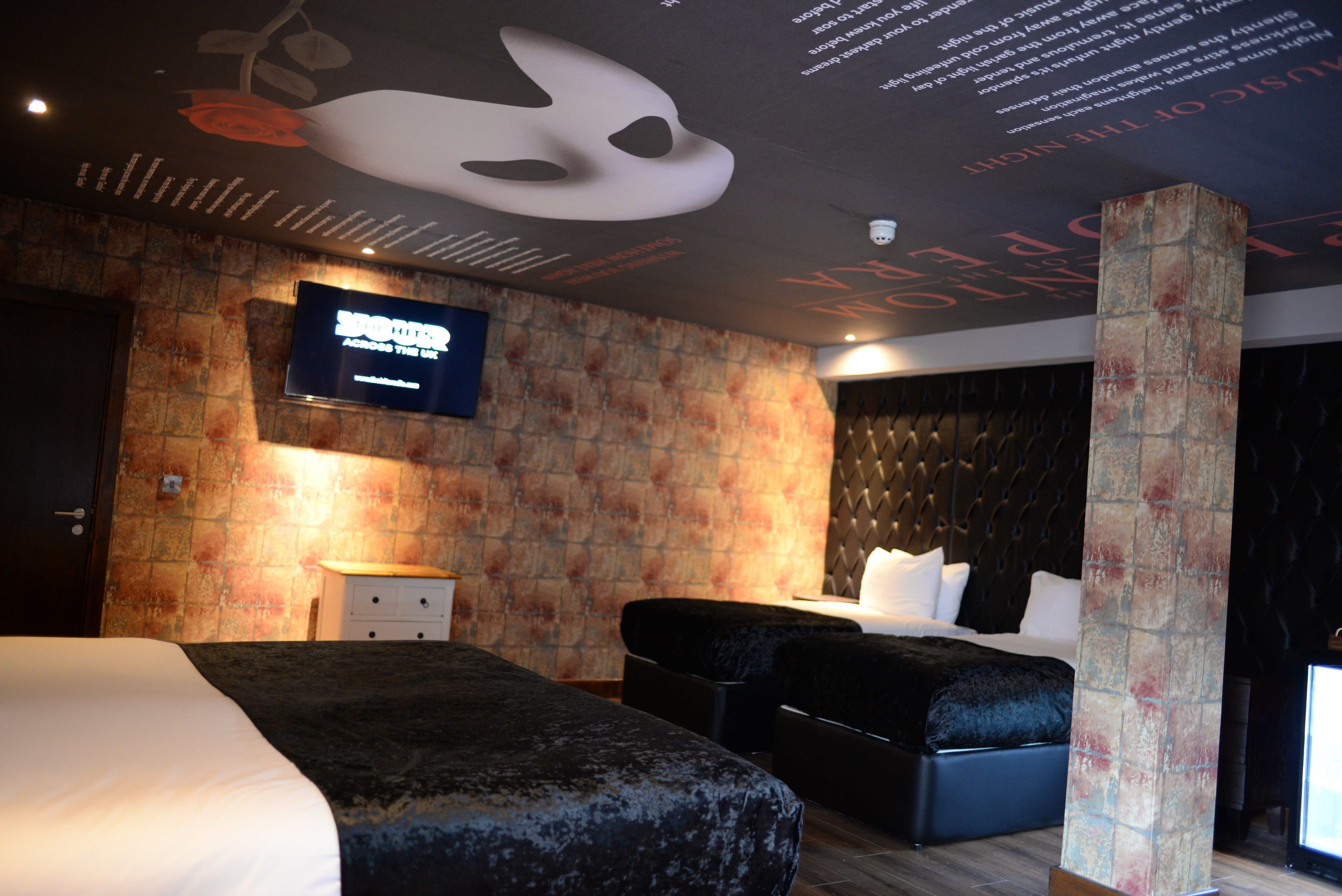 Habitación de hotel con una cama grande, una cama más pequeña, un televisor de pantalla plana, pared con textura de piedra y techo decorativo.