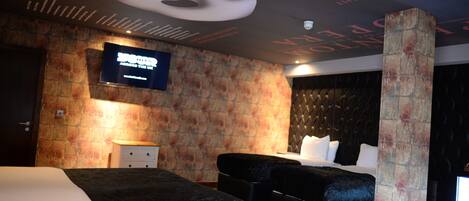 Habitación de hotel con una cama grande, una cama más pequeña, un televisor de pantalla plana, pared con textura de piedra y techo decorativo.