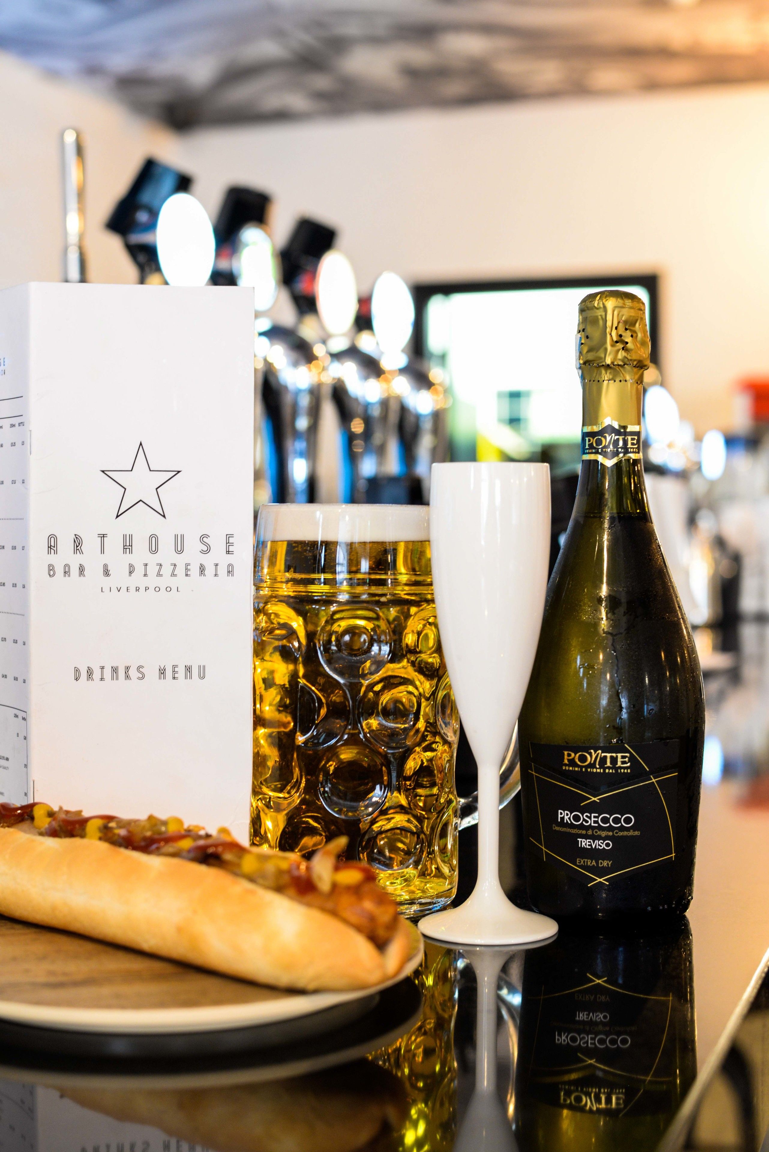 A menu at a bar and pizzeria with a bottle of Prosecco and a glass of beer on a table.