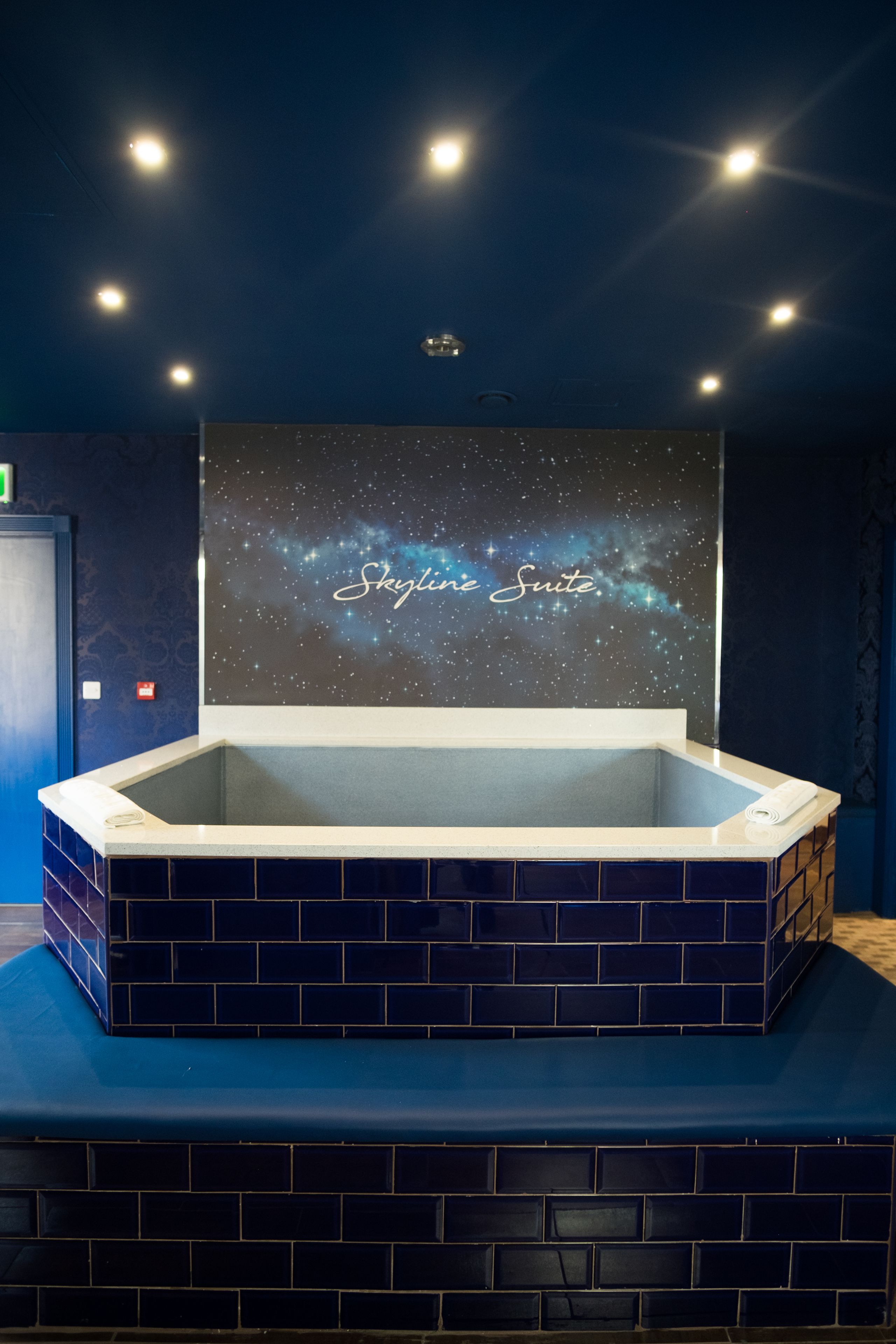 A hot tub with a 'Skyline Suite' sign above it, set against a dark blue wall with a starry sky mural.