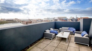 Une terrasse sur le toit avec des canapés gris, une table blanche et des coussins à motifs.