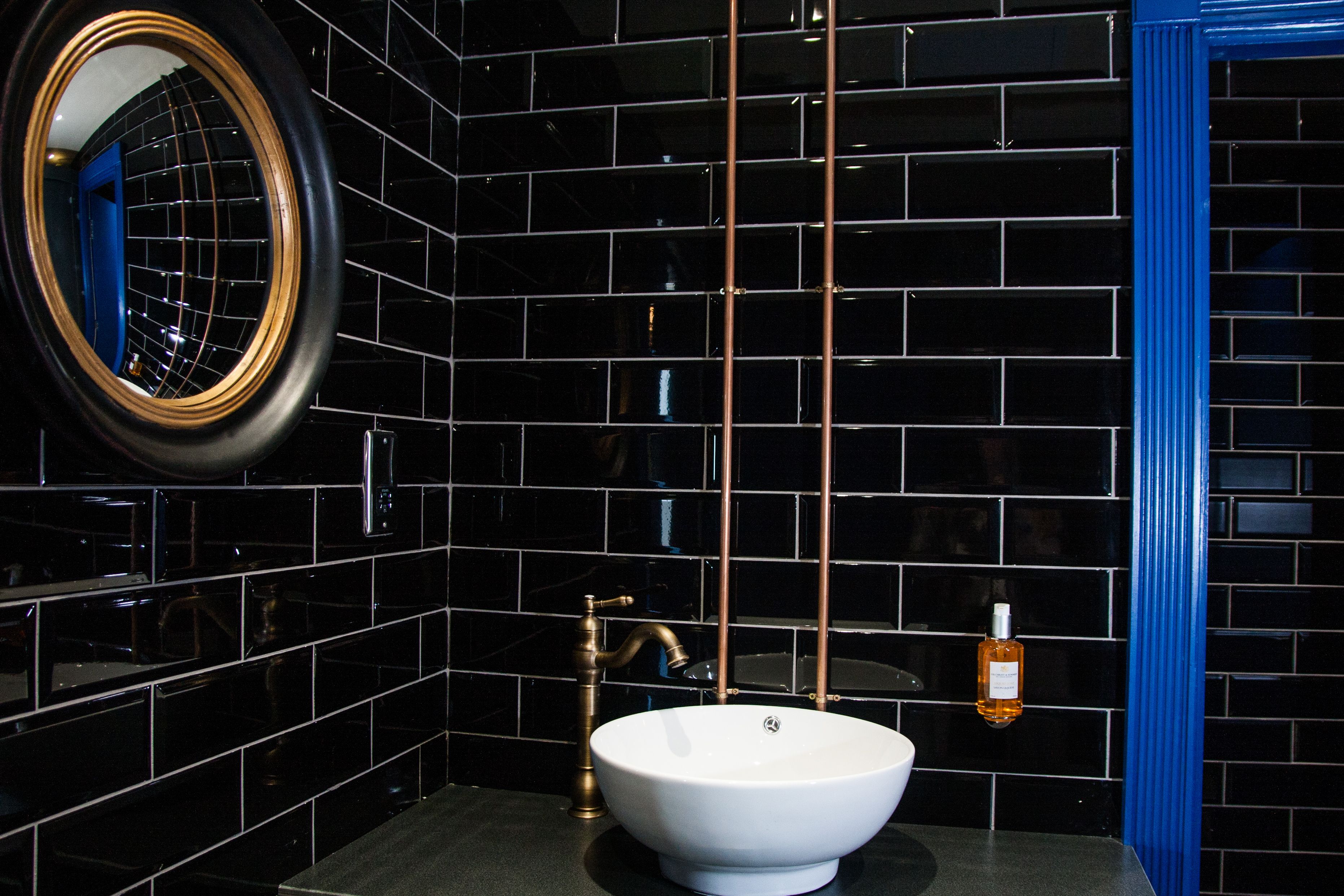 A bathroom with black tiled walls, a white sink, a round mirror, and a blue door.