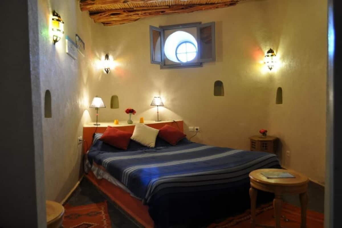 Un dormitorio pequeño y acogedor con una cama individual, dos lámparas de noche, una mesita y una ventana con vistas.