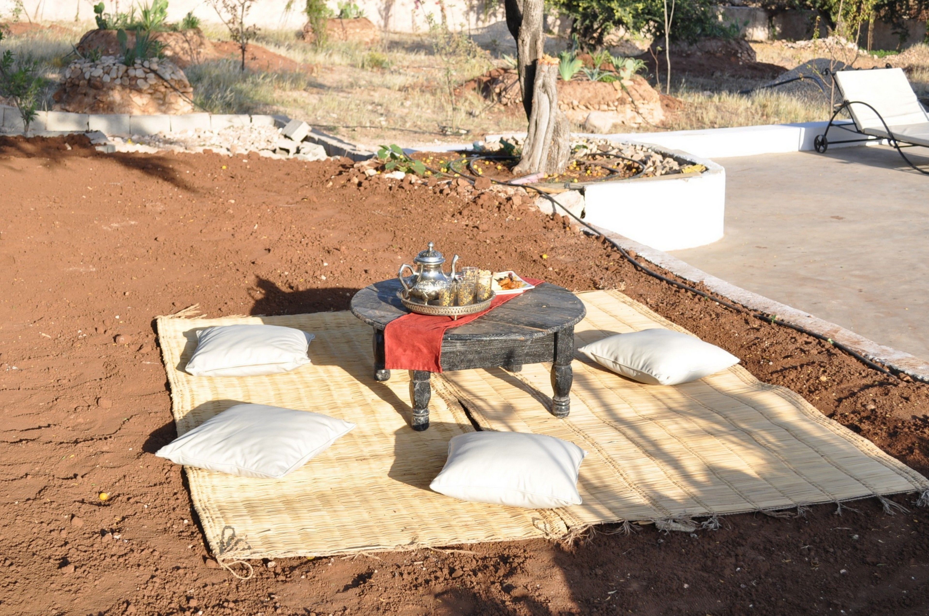 An outdoor dining area with a table set on a mat, surrounded by cushions.