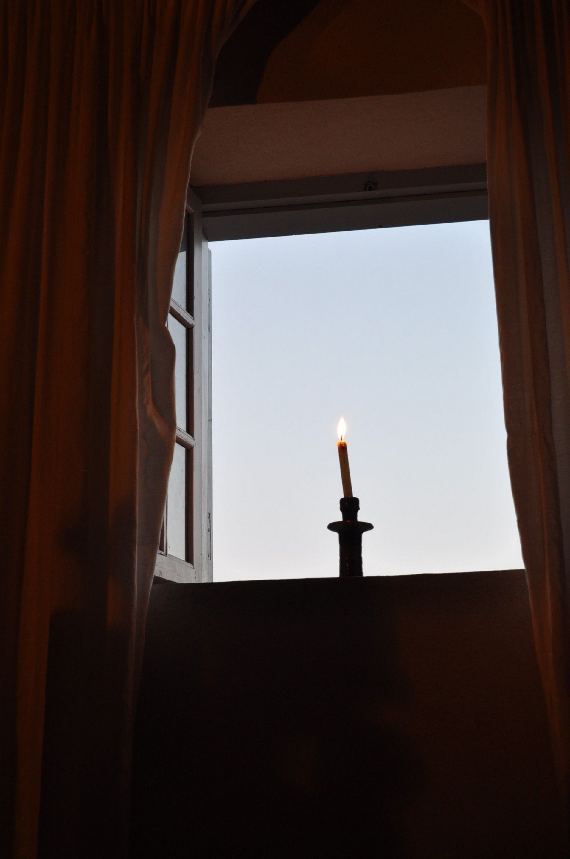 Ein Fenster mit einer brennenden Kerze im Inneren, umrahmt von Vorhängen.