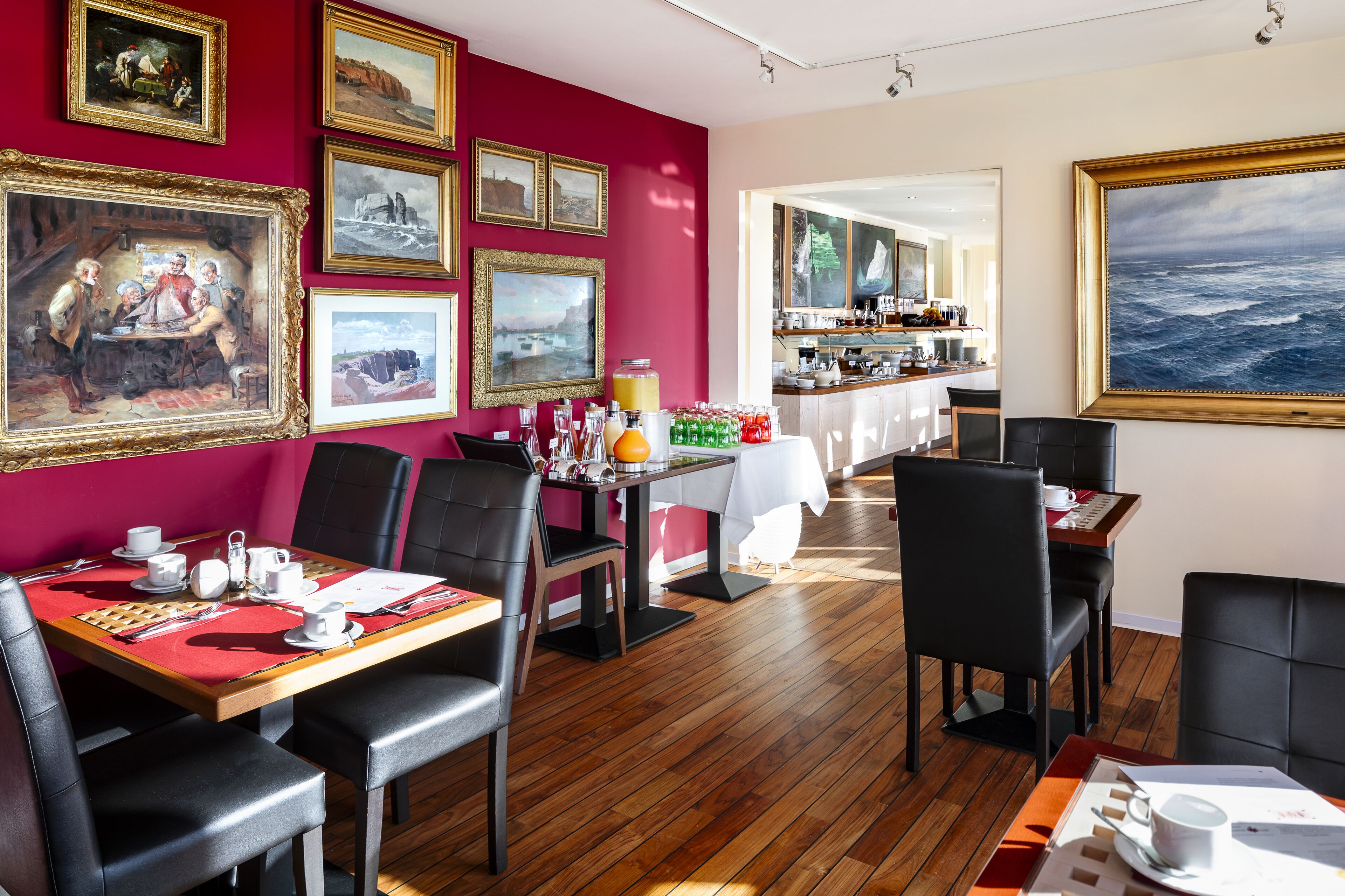 Un comedor con mesas de madera, sillas de cuero negro y paredes rojas decoradas con cuadros.