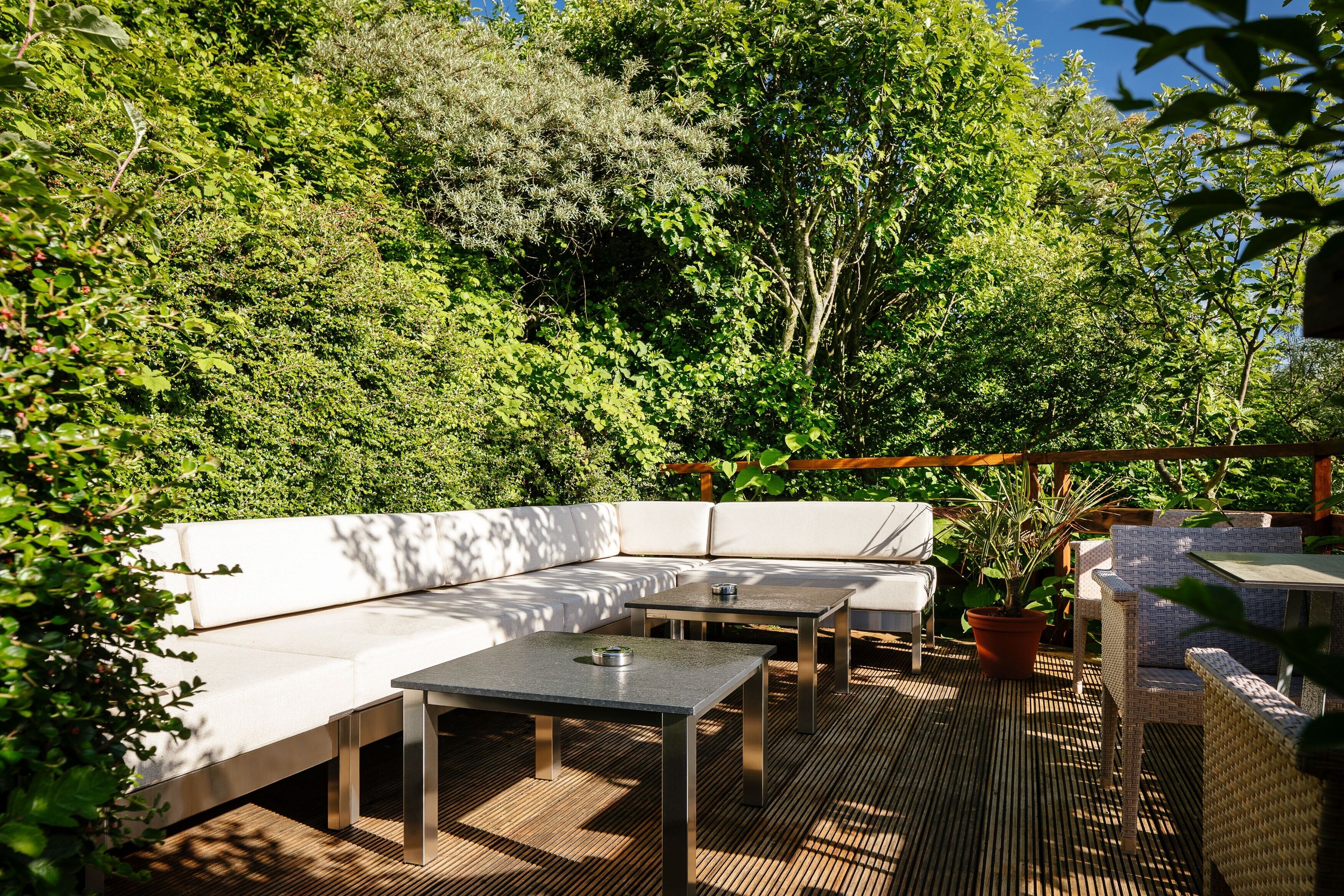 Un patio exterior con un sofá blanco, dos mesas y sillas de mimbre.