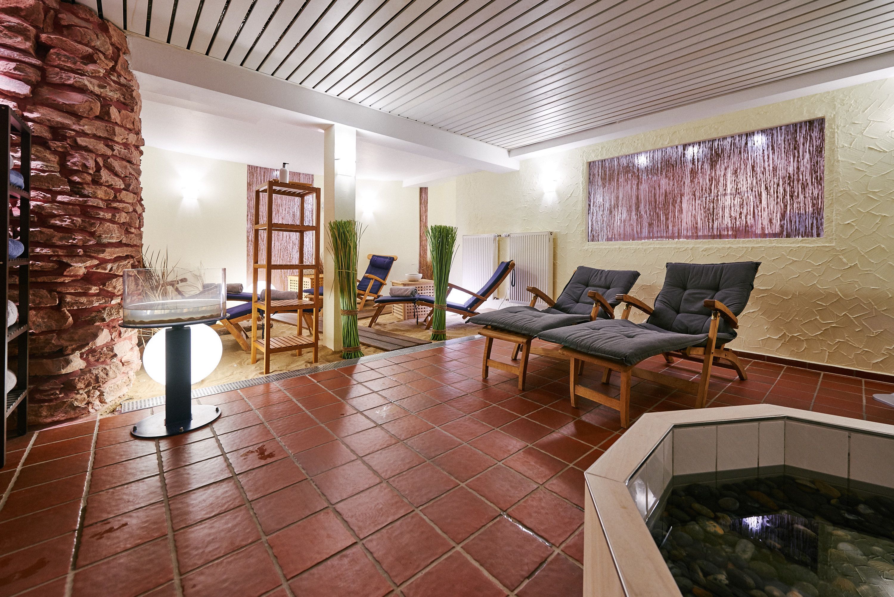 A spa area with a stone wall, a wooden chair, a massage table, and a hot tub.
