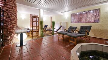 A spa area with a stone wall, a wooden chair, a massage table, and a hot tub.