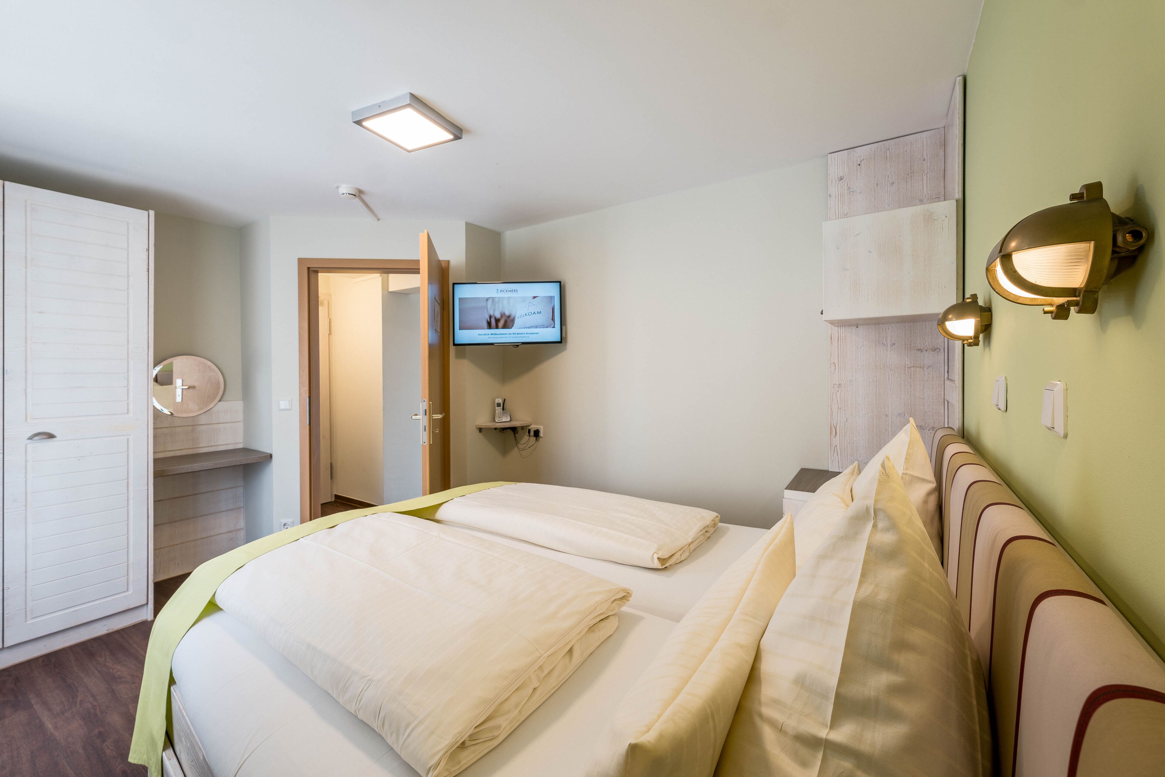 A hotel room with a bed, a television, a wall-mounted light fixture, and a wooden panel on the wall.